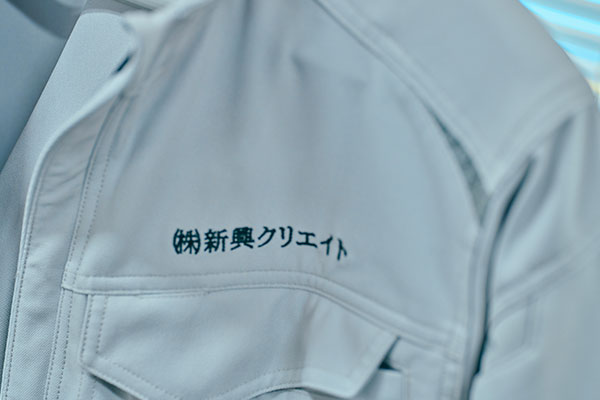 新興クリエイトの社名が入った作業着